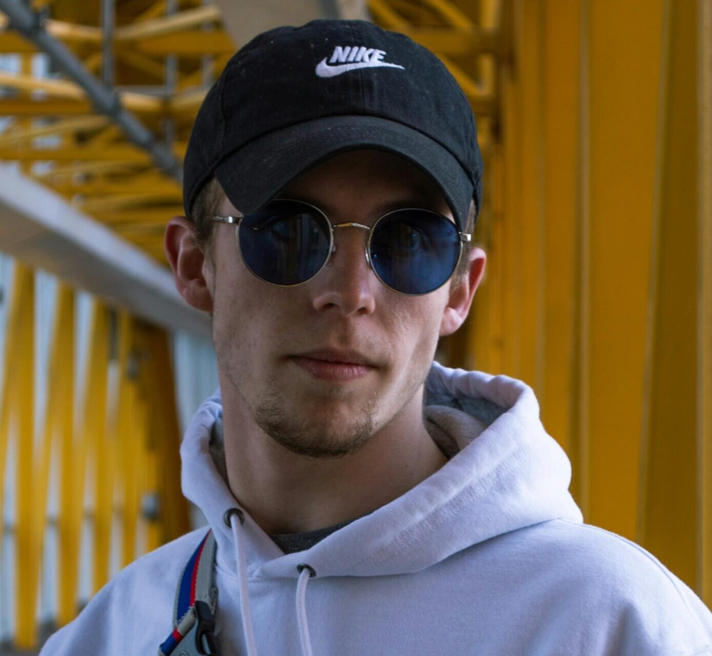 Young stylish man wearing sunglasses and hoodie standing outdoors. Urban fashion look.
